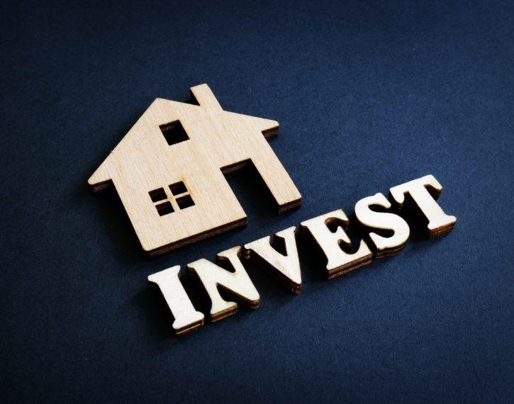 Word Invest and model of home from wood. Real Estate Investment concept.